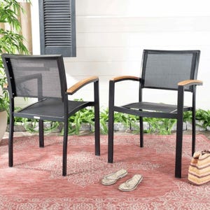May include: Two black outdoor chairs with mesh backs and wooden armrests are displayed on a red patterned rug. The chairs have a modern design. A pair of sandals and a striped tote bag are also visible.