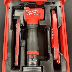 May include: A red and black Milwaukee M12 Fuel bandfile power tool with a battery pack, stored in a molded plastic carrying case. The tool features the text M12 BANDFILE at the top, with additional branding on the body and battery base.