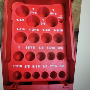 May include: A red tool organizer with multiple circular openings of varying sizes, labeled with fractional inch measurements like 7/16, 5/16, and 1/2. The organizer is designed to hold tools.