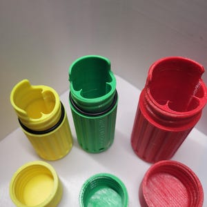 May include: Three 3D-printed containers in yellow, green, and red. Each container has a cylindrical body with a threaded interior and a matching lid. The containers are designed with a notched top and a black O-ring seal.