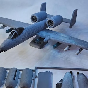 May include: A detailed, gray model airplane with two engines, wings, and a cockpit. The model includes several detachable components, such as additional engines and wing attachments. The plane is designed with realistic features and is likely a collectible or display item.