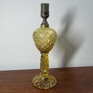May include: A vintage yellow glass lamp with a diamond pattern on the bulbous body and base. The lamp has a textured stem and a metal lamp holder at the top. The lamp is a decorative lighting fixture.