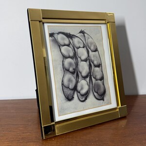 Peut inclure: Un cadre photo en métal doré avec une impression en noir et blanc de trois gousses de graines. Le cadre est de forme rectangulaire avec un design simple. L'impression est centrée dans le cadre.