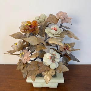 May include: A decorative bonsai-style sculpture featuring carved stone flowers in shades of white, pink, and amber. The flowers have delicate wire stamens with tiny beads, set among carved brown stone leaves on dark branches in a stone pot.