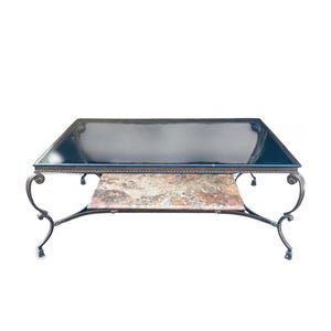 May include: A rectangular coffee table with a dark glass top and a lower shelf with a marble-like pattern. The table has ornate, curved metal legs and frame. The table is approximately 48 inches long and 24 inches wide.