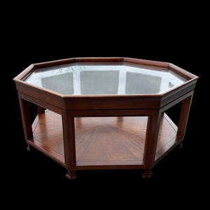 May include: An octagonal coffee table with a glass top and a lower shelf. The table is made of dark wood and has a classic design. The table is approximately 30 inches wide and 18 inches tall.