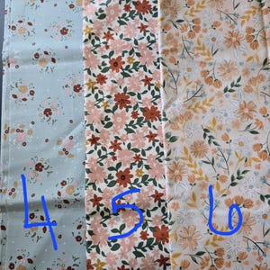 May include: Three fabric swatches with floral patterns. The first is a light blue with small pink and brown flowers. The second has pink and rust-colored flowers with green leaves. The third features peach and white flowers on a cream background.