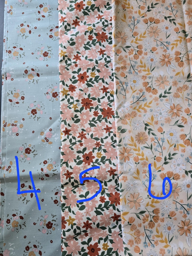 May include: Three fabric swatches with floral patterns. The first is a light blue with small pink and brown flowers. The second has pink and rust-colored flowers with green leaves. The third features peach and white flowers on a cream background.