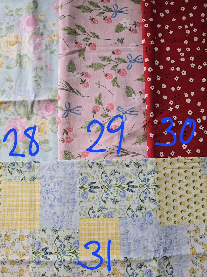 May include: Assortment of fabric swatches featuring floral and fruit patterns. Includes a light blue fabric with roses, a pink fabric with strawberries, and a red fabric with white flowers. Also includes a patchwork design with yellow and blue patterns.