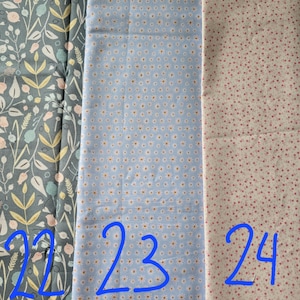 May include: Three fabric swatches with different patterns. The first is a dark teal with a floral design. The second is light blue with small white and yellow flowers. The third is off-white with small pink dots. Numbers 22, 23, and 24 are written in blue.