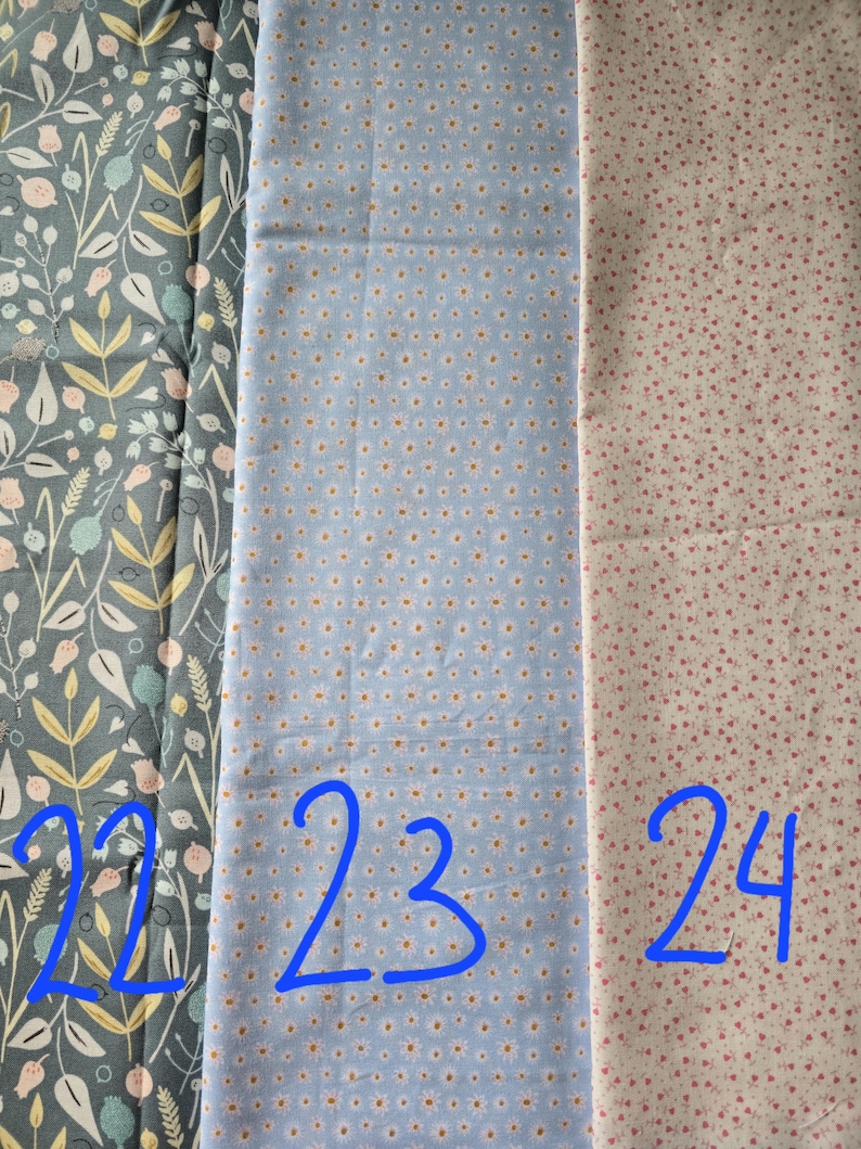 May include: Three fabric swatches with different patterns. The first is a dark teal with a floral design. The second is light blue with small white and yellow flowers. The third is off-white with small pink dots. Numbers 22, 23, and 24 are written in blue.