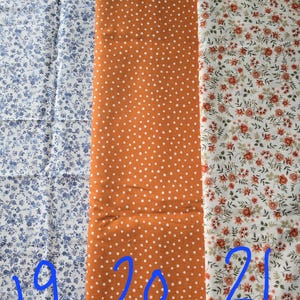 May include: Three fabric swatches with different patterns. The first is white with blue floral designs. The second is orange with white polka dots. The third is white with red and green floral patterns. Numbers 19, 20, and 21 are written on the fabrics.