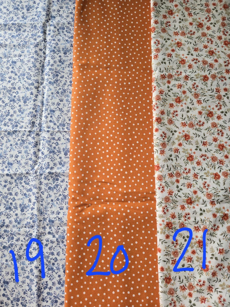 May include: Three fabric swatches with different patterns. The first is white with blue floral designs. The second is orange with white polka dots. The third is white with red and green floral patterns. Numbers 19, 20, and 21 are written on the fabrics.