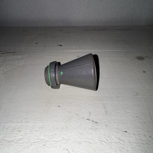 May include: A gray, conical-shaped plastic nozzle attachment featuring a threaded base and a thin, bright green rubber O-ring seal. The component has a smooth, matte finish and a small green dot marking on its side, designed for fluid flow.