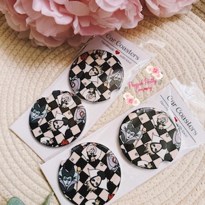 May include: Four car coasters with a black and white checkered pattern and images of Disney villains. Each coaster is packaged and labeled "Car Coasters Handmade with love". The brand name "Pressed Pretty Company" is also visible.