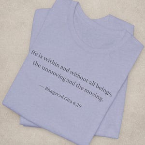 May include: A light purple t-shirt with the quote "He is within and without all beings, the unmoving and the moving. - Bhagavad Gita 6.29" printed in dark gray. The shirt is folded.