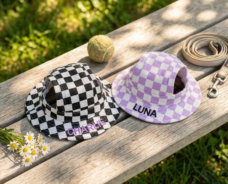 May include: Two pet hats with a checkered pattern, one black and white, the other lavender and white. The black and white hat has the name "CHARLIE" embroidered on it, and the lavender hat has "LUNA" embroidered on it.