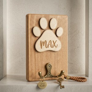 May include: Wooden key holder with a paw print design and the name "MAX" engraved. Features a brass hook with keys and a dog tag that says "RUBY". A braided leather keychain is attached.