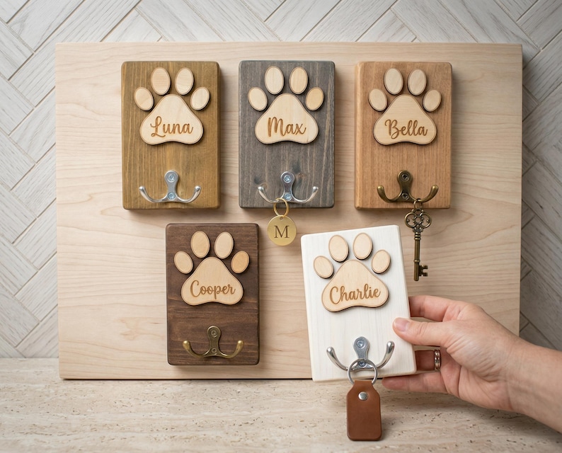 May include: Wooden key holder with paw print design. The key holders are in various colors, including light brown, gray, and dark brown. Each key holder has a paw print and a name, such as Luna, Max, Bella, Cooper, and Charlie.