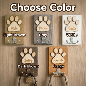 May include: Wooden pet leash holders in light brown, gray, white, dark brown, and orange. Each features a paw print design with a name and a double hook. The text "Choose Color" is at the top.
