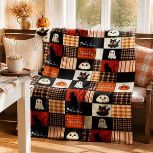 Könnte beinhalten: Eine rechteckige Wohndecke mit einem Patchwork-Design aus schwarzen, orangefarbenen und weißen Quadraten. Das Muster zeigt Illustrationen von schwarzen Katzen, weißen Geistern, Kürbissen und dem Wort Spooky, durchsetzt mit karierten und gestreiften Stoffblöcken.