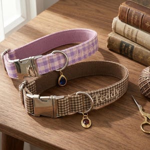 May include: Two personalized dog collars with metal buckles and charms. One is lavender gingham with "Angie" embroidered, the other is brown gingham with "Teddy" embroidered. Accessories include vintage books, twine, and scissors.