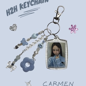 Puede incluir: Un llavero decorativo con una foto de Carmen, adornado con cuentas azules, una flor y un dije de mariposa. También presenta el texto "H2H KEYCHAIN".