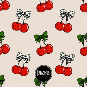May include: A repeating pattern on a light beige grid background featuring pairs of bright red cherries with green stems. Some cherries are accented with white bows featuring green polka dots, while others have solid green bows. Text reads DUCKIE. DESIGN STUDIO.