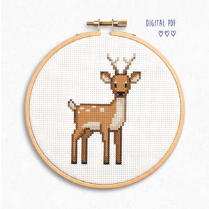 Könnte beinhalten: Kreuzstich-Stickerei eines Hirsches in einem Holzreifen. Der Hirsch ist braun mit weißen Flecken und Geweih. Der Text "DIGITAL PDF" und drei Herzen befinden sich in der oberen rechten Ecke.