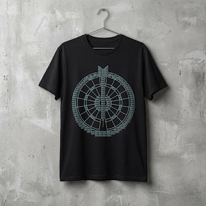 May include: Black t-shirt featuring a teal dartboard graphic with text. The design is centrally placed on the shirt. The t-shirt is suspended on a metal hanger against a grey concrete wall.
