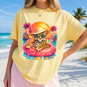 Peut inclure: T-shirt jaune clair avec un motif de léopard portant des lunettes de soleil et un chapeau de soleil, flottant dans une bouée rose. Le motif comprend des palmiers, des flamants roses et un coucher de soleil. Thème estival et plage.