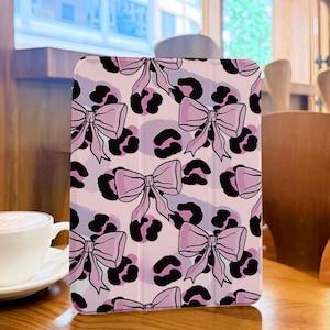 May include: A pink tablet case featuring a repeating pattern of pink bows and black leopard spots. The case is designed to protect a tablet and adds a stylish touch with its playful design.