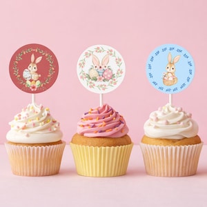May include: Four cupcakes with pastel frosting and decorative toppers. Each topper features a different Easter bunny design in a circle. The cupcakes have yellow and peach-coloured liners, with sprinkles.