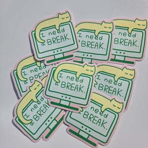 May include: A collection of die-cut stickers featuring a pale yellow cat resting on top of a computer monitor. The screen displays the text I need a BREAK in dark green lettering. Each sticker has a light pink border and a green monitor frame.