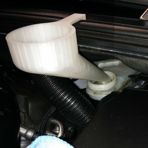 May include: A white plastic funnel is used to pour a liquid into a car's reservoir. The funnel has a wide mouth and a long, tapered spout. The reservoir is white and has a screw-on cap. The engine compartment is black.