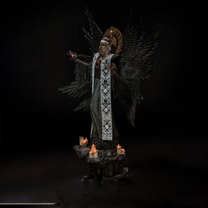 May include: A dark-winged figure wearing a long black robe with a white embroidered stole and a gold halo, standing on a rocky base surrounded by small lit candles. The figure has a mask covering the lower face and large feathered wings.