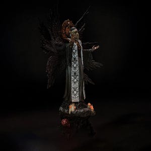 May include: A dark-toned figurine of a winged entity wearing a plague doctor mask and a long robe with a white floral patterned stole. The figure stands on a rocky base with small lit candles, featuring large black wings and a circular halo.