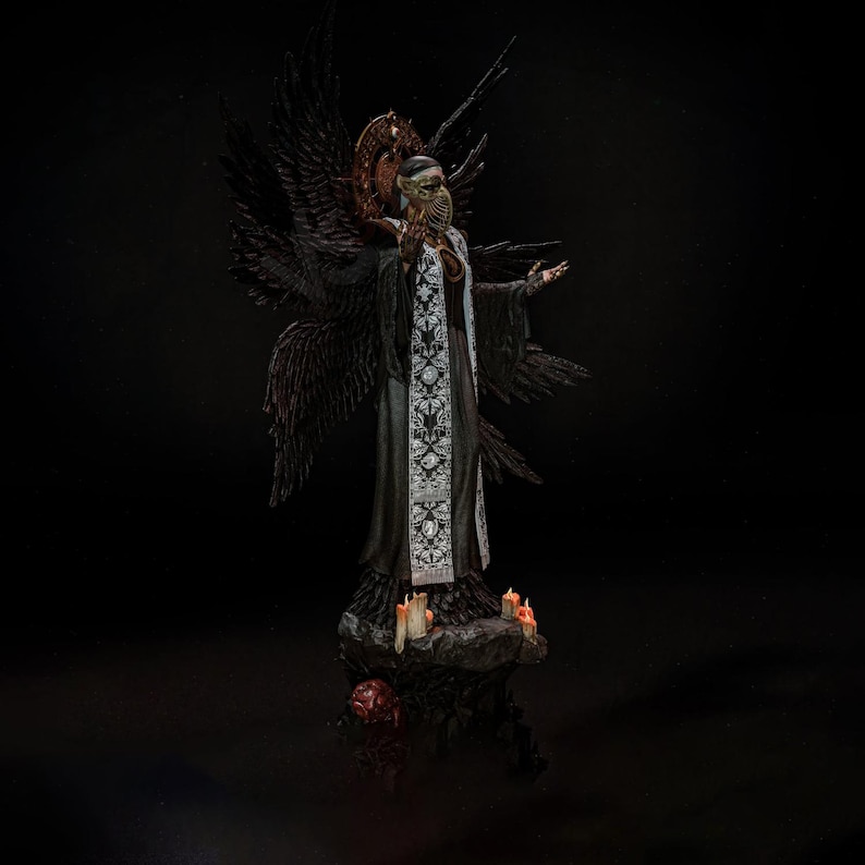May include: A dark-toned figurine of a winged entity wearing a plague doctor mask and a long robe with a white floral patterned stole. The figure stands on a rocky base with small lit candles, featuring large black wings and a circular halo.