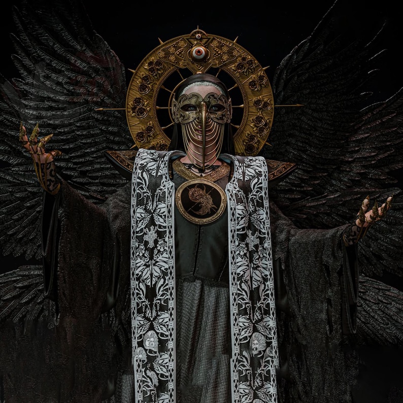 May include: A dark costume featuring large black feathered wings, a gold halo headpiece with a central eye, and a metallic plague doctor mask. The attire includes a black robe with a white patterned stole and a circular chest emblem with gold details.