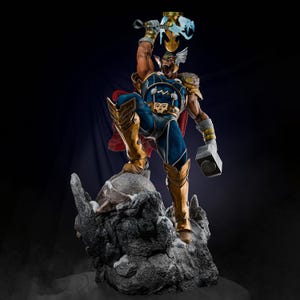 Op de afbeelding: Gedetailleerd beeldje van een superheld in een dynamische pose, gekleed in een blauw en goud kostuum met een rode cape. Het beeldje houdt een gloeiende hamer vast en staat op een rotsachtige basis, met een donkere achtergrond.