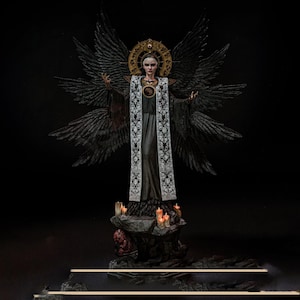 May include: A detailed figurine of a figure with large black wings, wearing a long black robe and a white embroidered stole. The figure has a gold halo behind the head and stands on a rocky base decorated with several small, lit orange candles.