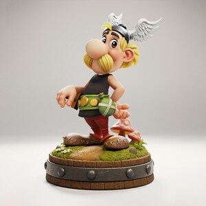 Op de afbeelding: Gedetailleerd beeldje van Asterix, een stripfiguur, staat op een houten voet met een paddenstoel. Hij draagt een zwart topje, een rode broek en een groene riem met een tasje. Zijn helm heeft vleugels en hij heeft een grote neus en een gele snor.