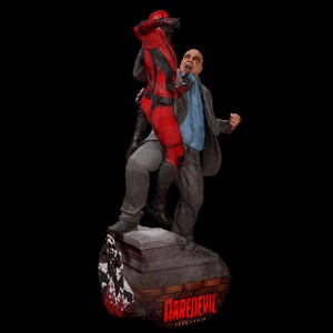 Op de afbeelding: Een gedetailleerd beeld dat een vechtscène uitbeeldt. Eén figuur draagt een rood en zwart pak, de ander een pak en een blauw overhemd. De basis leest "Daredevil Born Again" met een bakstenen ontwerp.