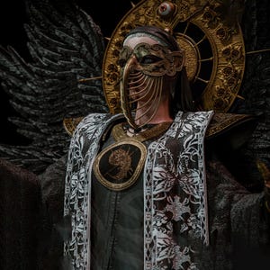 May include: A figure wearing an ornate gold filigree mask with a beak-like nose piece, a dark robe with white lace trim, and a large circular gold halo featuring a central eye. The figure has dark feathered wings and a circular chest emblem.