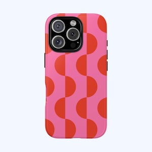 May include: A pink phone case with a repeating pattern of orange half-circles. The case has a glossy finish and a black camera module. The design is a retro, geometric style.