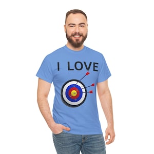 Op de afbeelding: Lichtblauw T-shirt met de tekst "I LOVE" boven een doelwit met drie pijlen. Het doelwit is veelkleurig met rode, gele, blauwe en witte ringen. De pijlen zijn rood met witte veren.