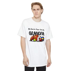 May include: White t-shirt with the text "My favorite Player Calls Me GRANDPA" in black. Below the text are illustrations of a football, basketball, soccer ball, and other sports balls. The shirt is worn by a person.