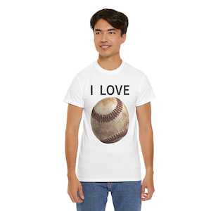 Op de afbeelding: Wit T-shirt met de tekst "I LOVE" boven een honkbalafbeelding. De honkbal is bruin en wit met rode stiksels. Het shirt is een casual stijl.