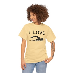 Op de afbeelding: Een lichtgeel t-shirt met de tekst "I LOVE" boven een zwart silhouet van een zwemmer in het water. Het shirt is gemaakt van een zacht materiaal en wordt door een persoon gedragen.