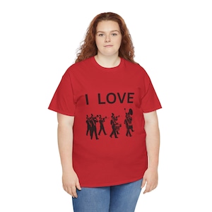 Op de afbeelding: Rood T-shirt met de tekst "I LOVE" en een zwart silhouet van een marching band die instrumenten bespeelt. Het T-shirt wordt door een persoon gedragen. Het ontwerp is op de voorkant gedrukt.